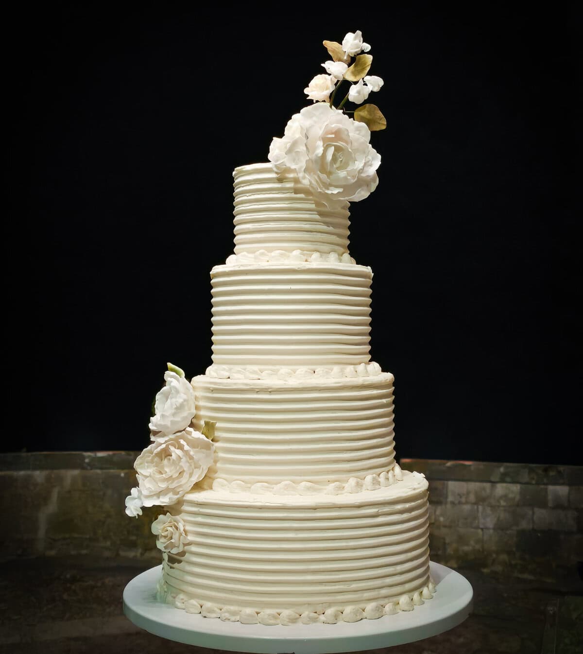 Four-tier buttercream wedding cake with piped pearl borders and handcrafted sugar roses at Castello Il Palagio in Tuscany, Italy.
