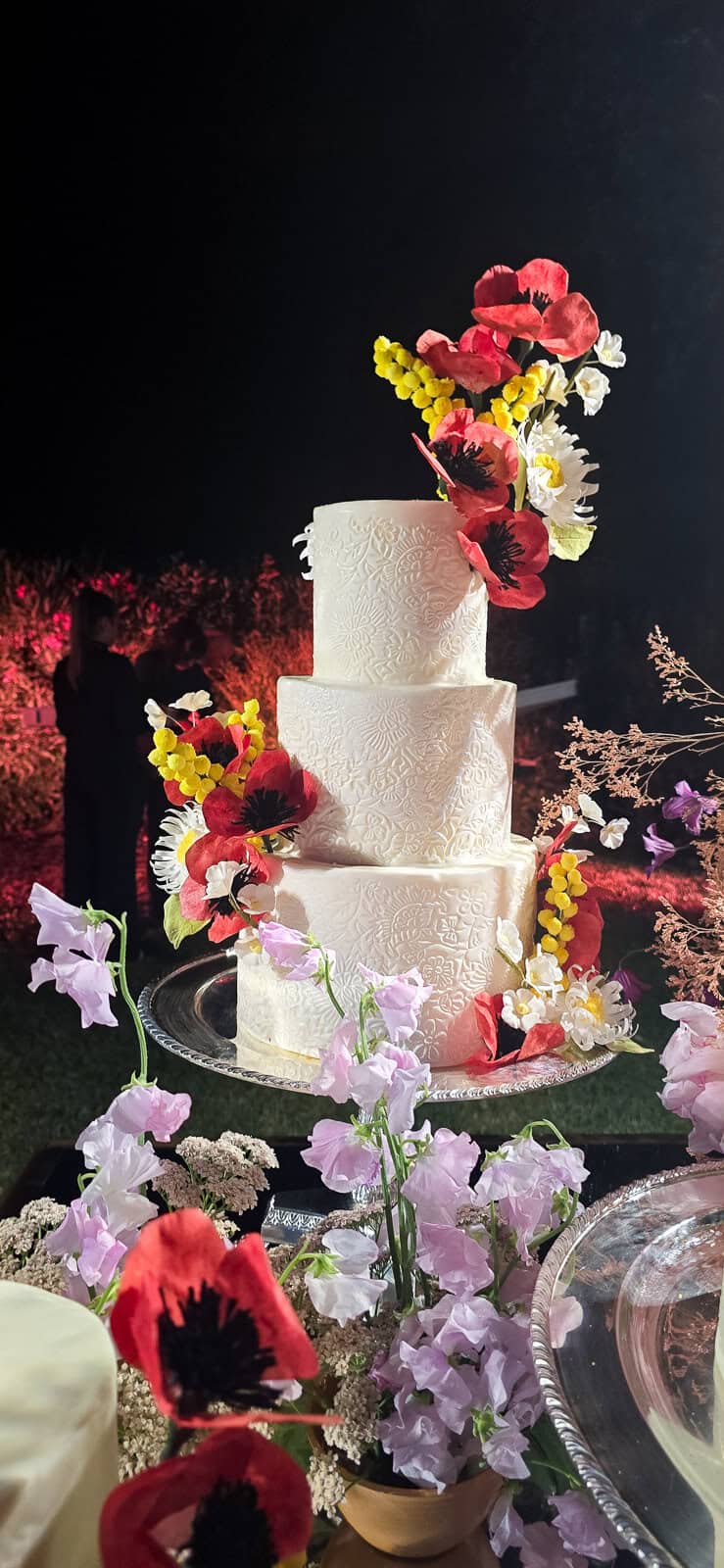 Textured white tiered wedding cake with sugar poppies, sugar daisies, and sugar mimosa at L’Andana Resort in Badia, Castiglione della Pescaia, Tuscany.