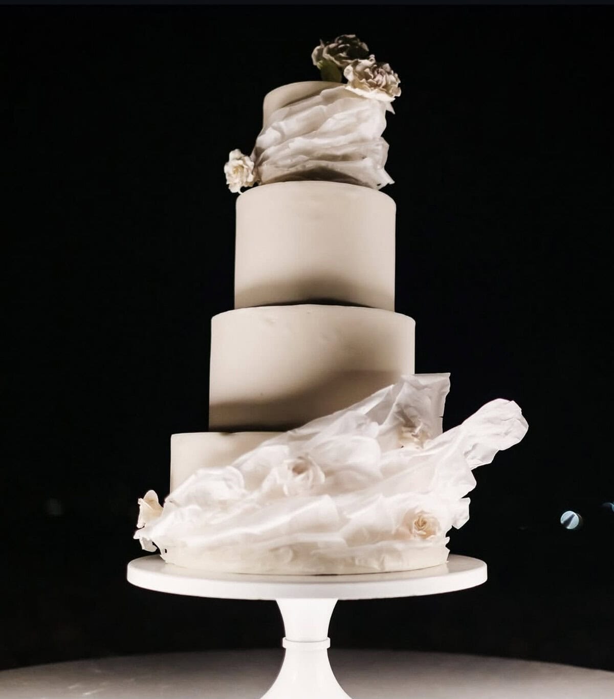 Modern white tiered wedding cake with sculptural draped design and delicate floral accents.