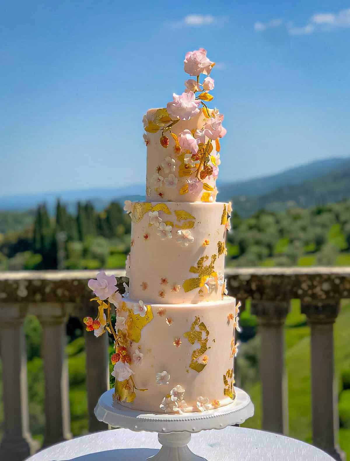 Pink tiered wedding cake with gold leaf and handcrafted sugar flowers at a castle near Florence, Tuscany, Italy.