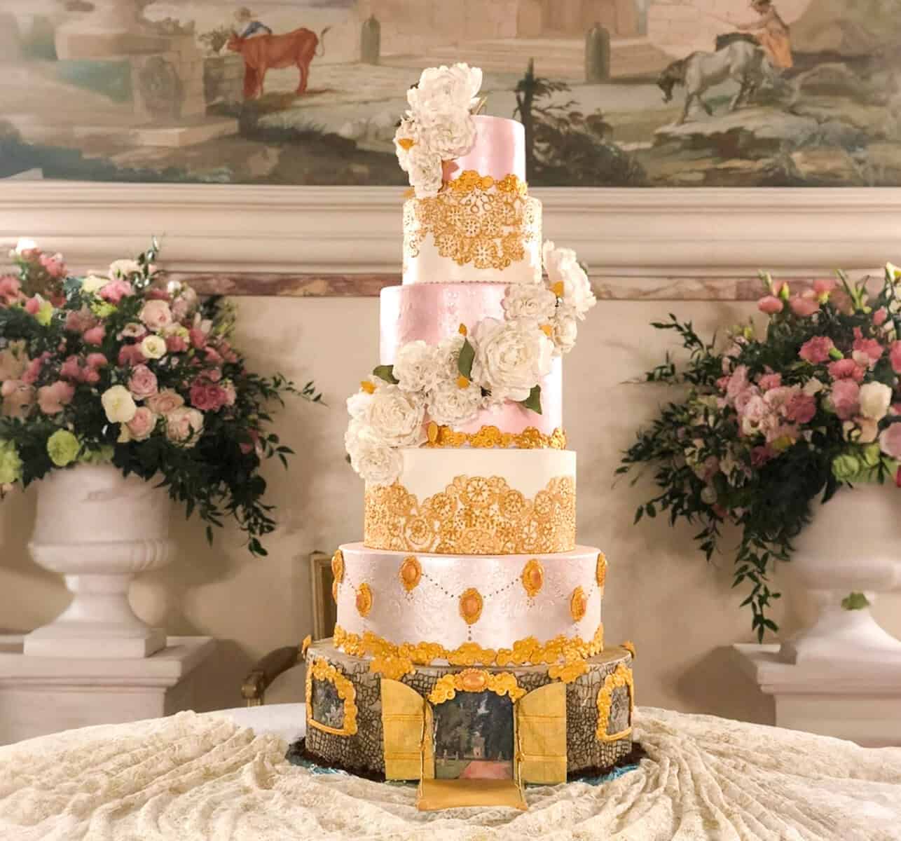 Luxury princess castle wedding cake with pink tiers, gold lace detailing, and white sugar flowers for a destination wedding in Italy.