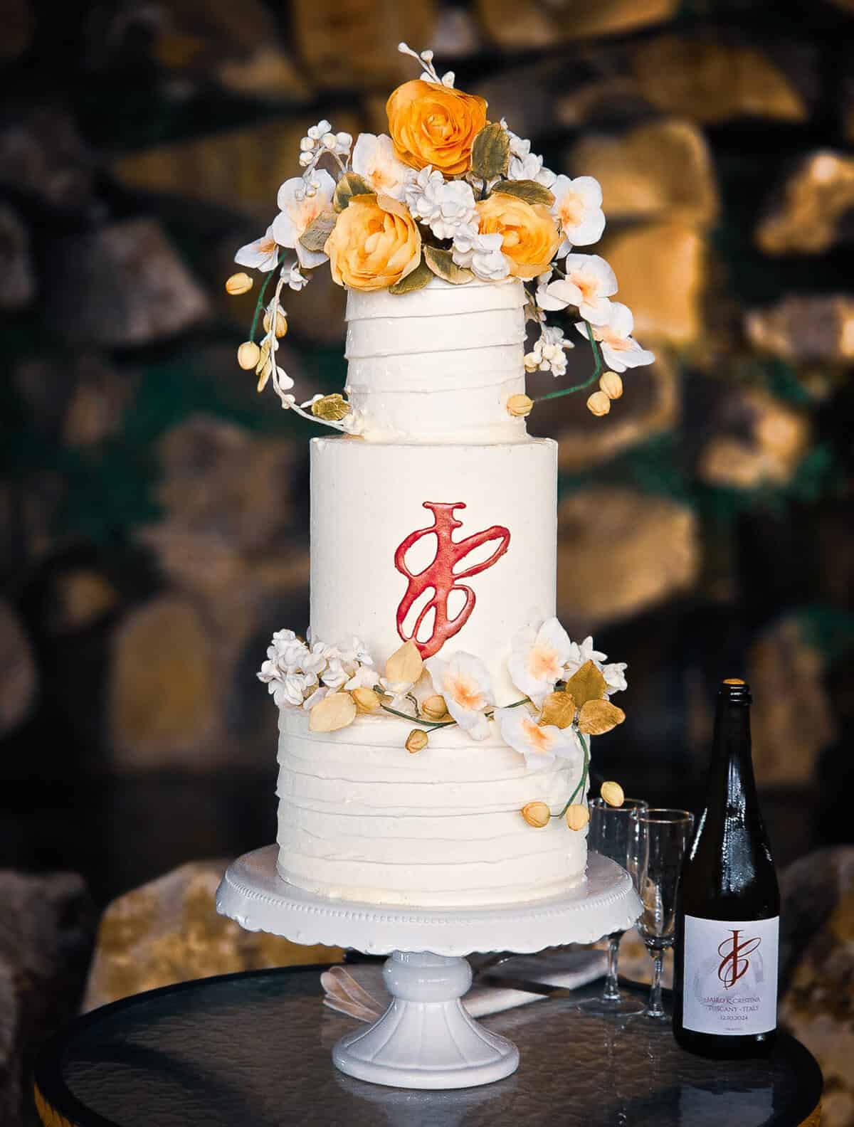 Tall white buttercream wedding cake, perfect for fall wedding with a red monogram and orange sugar flowers at a castle in Tuscany, Italy.