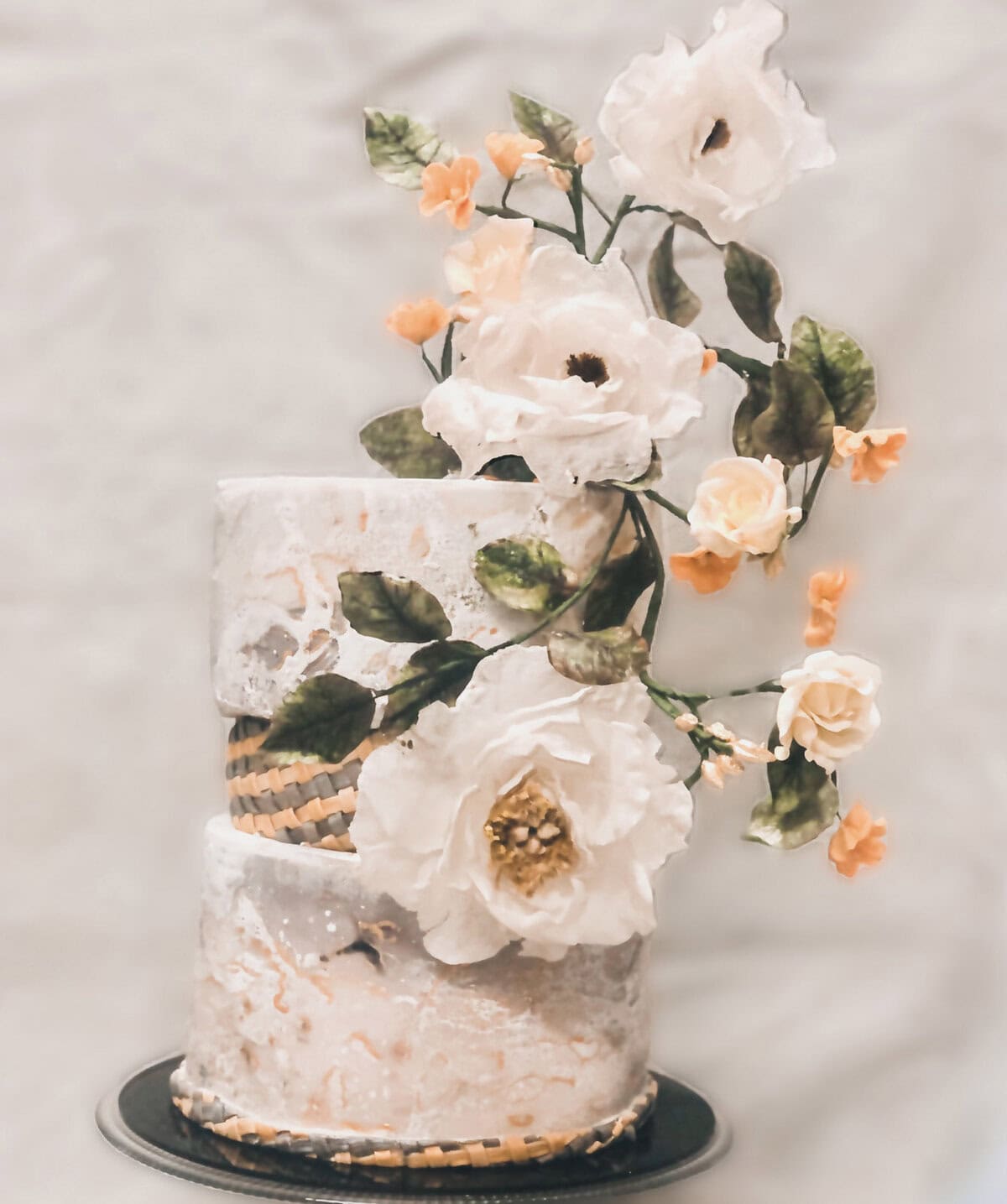 Modern marble-effect wedding cake with a braided band detail and cascading sugar flowers in white and peach tones in Tuscany, Italy.