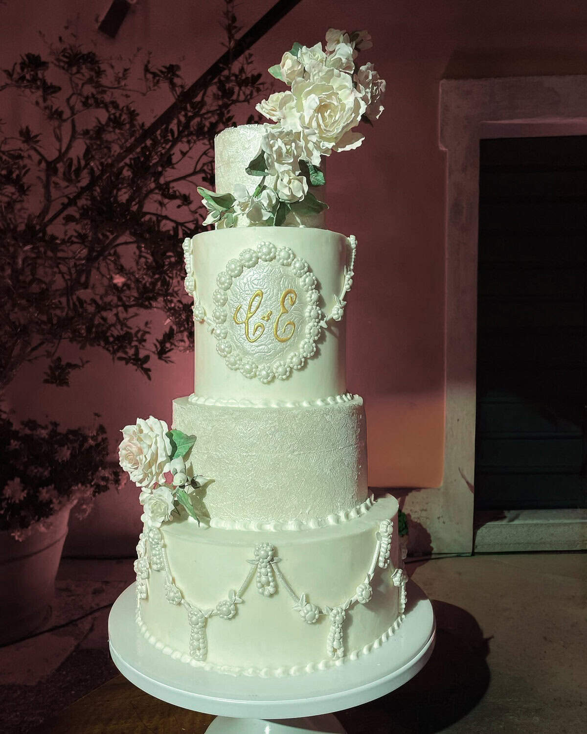 Luxury white tiered wedding cake with monogram crest, pearl swag piping, and sugar roses at Villa Centinale in Tuscany, Italy.