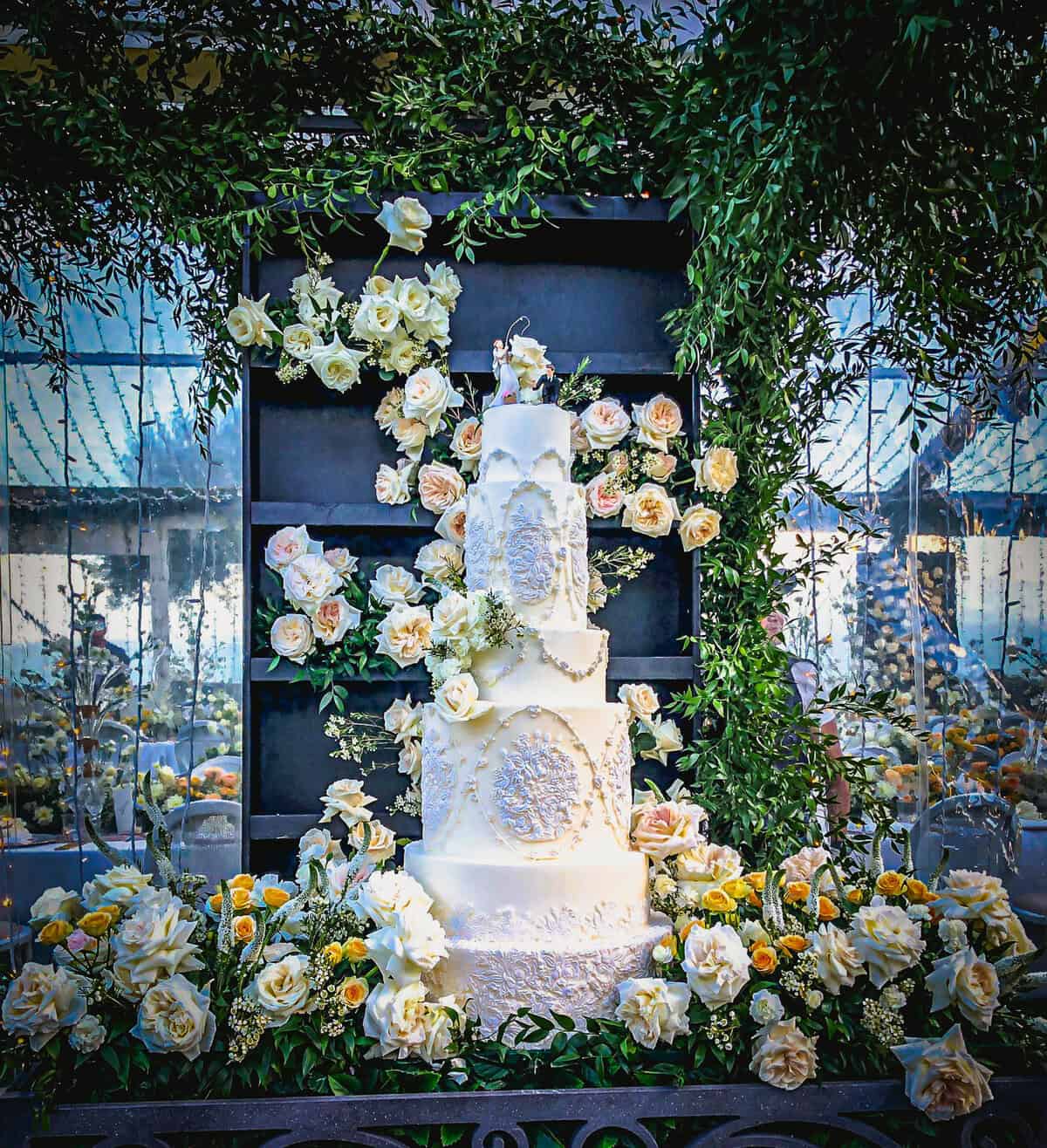 Monumental ivory tiered wedding cake with intricate piping and bas-relief medallion details, styled with roses and greenery at Villa Cimbrone in Ravello on the Amalfi Coast, Italy.