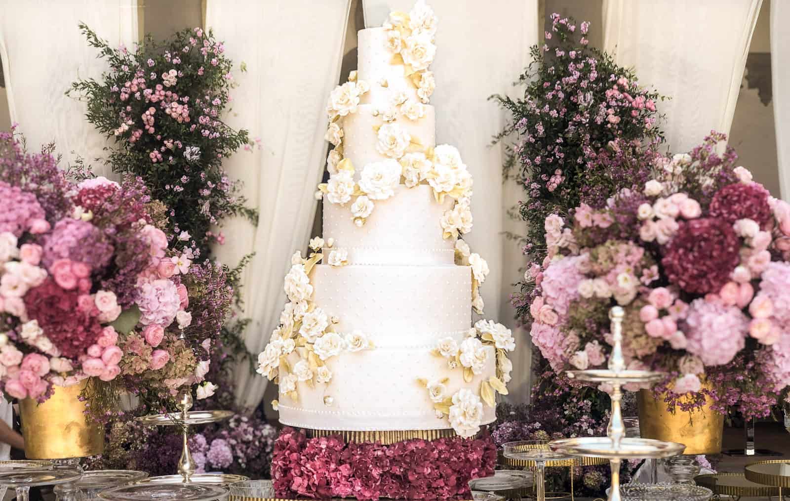 Luxury white tiered wedding cake with cascading white sugar roses and gold leaf at Villa Collazzi near Florence, Tuscany, Italy.