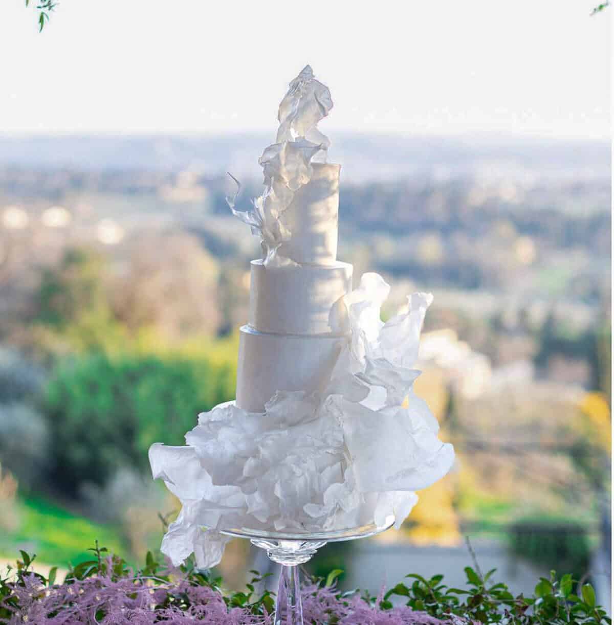 Dramatic white wedding cake with sculptural wafer paper ruffles overlooking Tuscany at Villa Fontanelle, Italy.