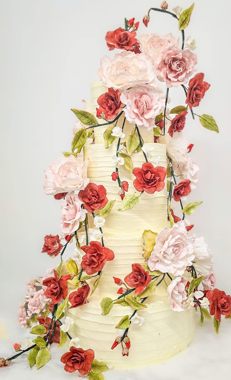 Tall buttercream birthday cake with cascading red and blush sugar roses at Villa Miani in Rome, Italy.