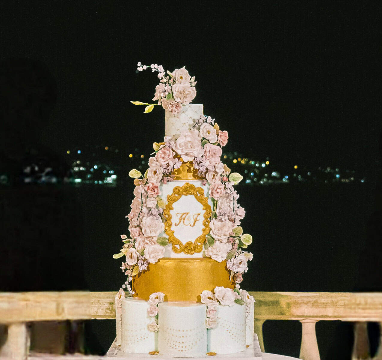 Tall tiered wedding cake with blush sugar flowers, a gold tier, and a monogram plaque at Villa Pliniana on Lake Como, Italy.