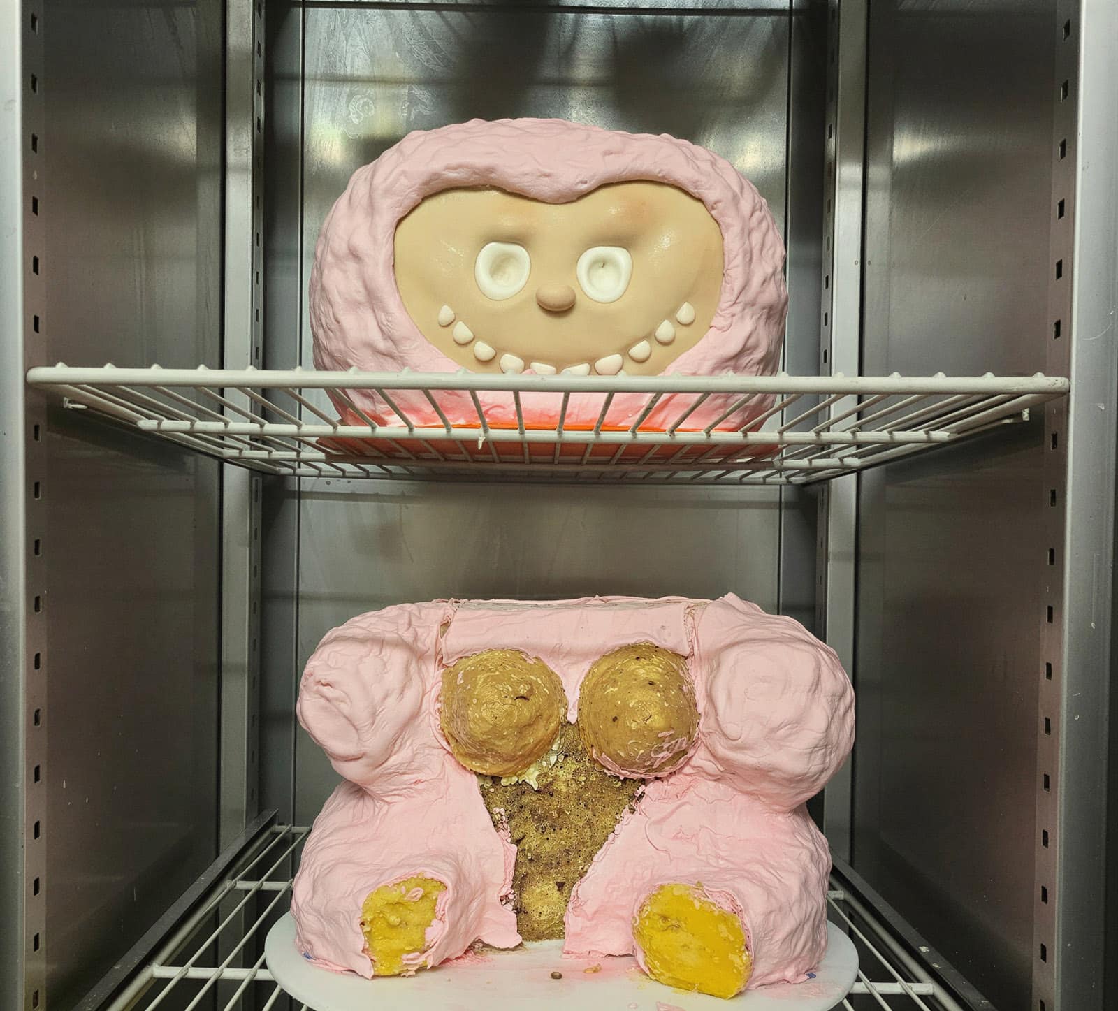 Labubu birthday cake head and body in progress in a refrigerator after the first coat of pink.