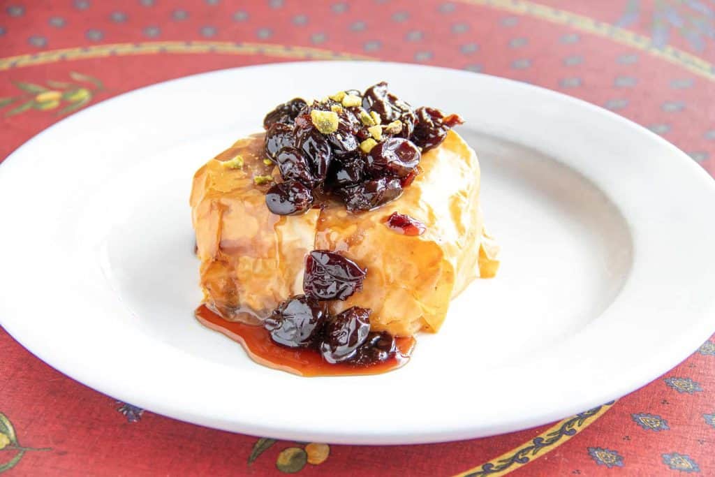 Baked Brie cheese with berry compote and crushed pistachios on a white plate.