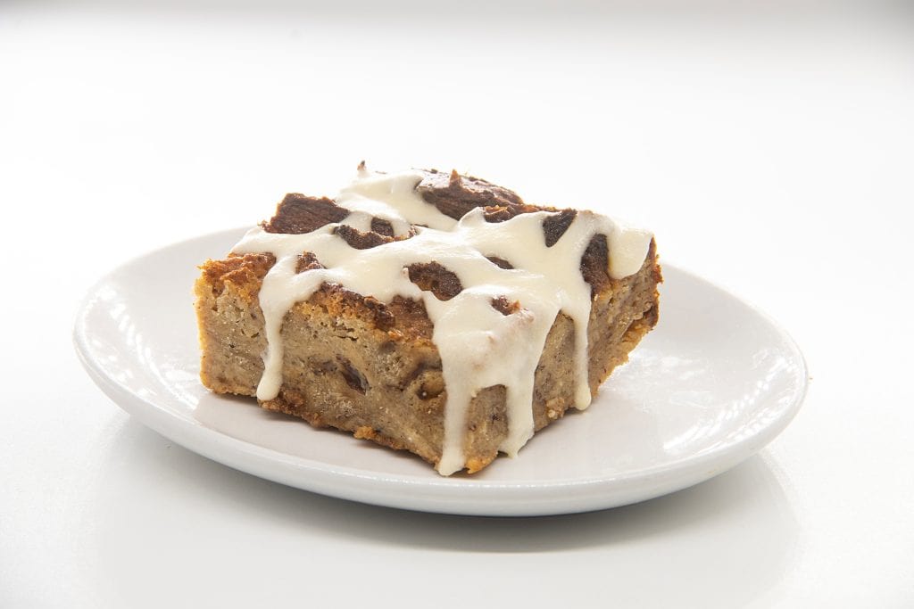 Chocolate chip cookie bar with white icing on a white plate.