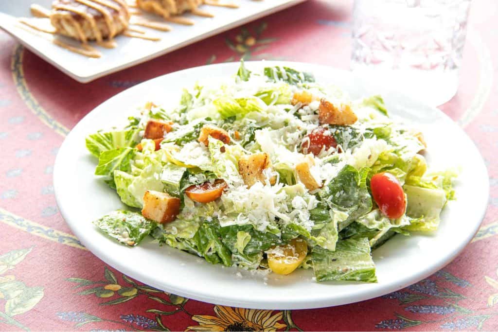 Fresh Caesar Salad with croutons, cherry tomatoes, and grated cheese on a white plate.