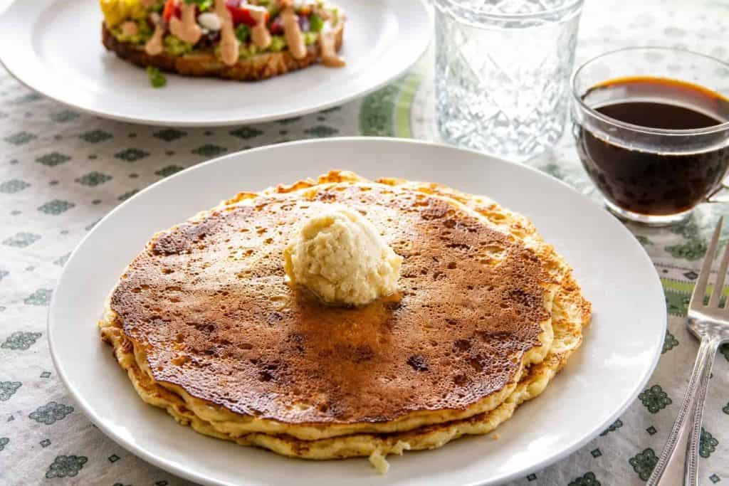 Delicious apple cinnamon pancakes with butter and syrup on a white plate.