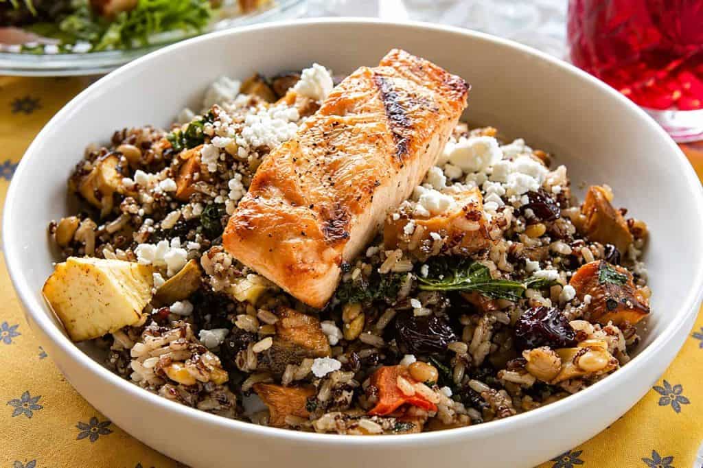 Salmon fillet on a grain bowl with vegetables and cheese.