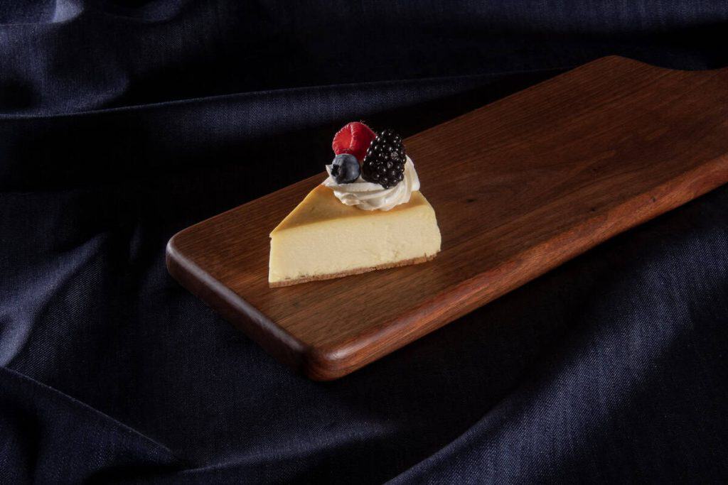 Delicious cheesecake slice topped with berries on wooden serving board.