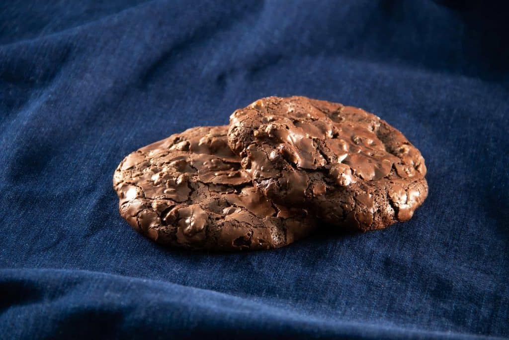 Two gluten and dairy free chocolate cookies on dark fabric.