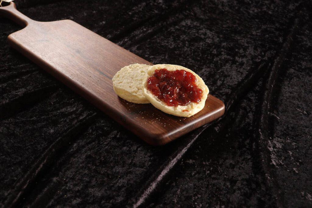 English muffin sliced in half with strawberry jam on a wooden board.
