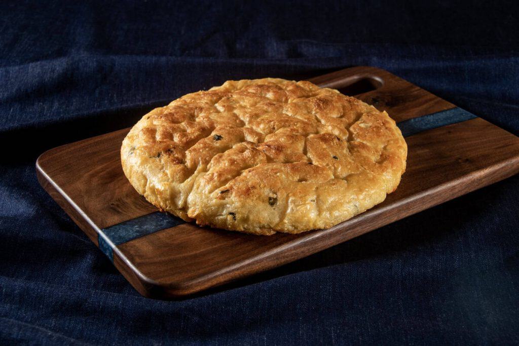 Golden baked focaccia bread on wooden serving board.