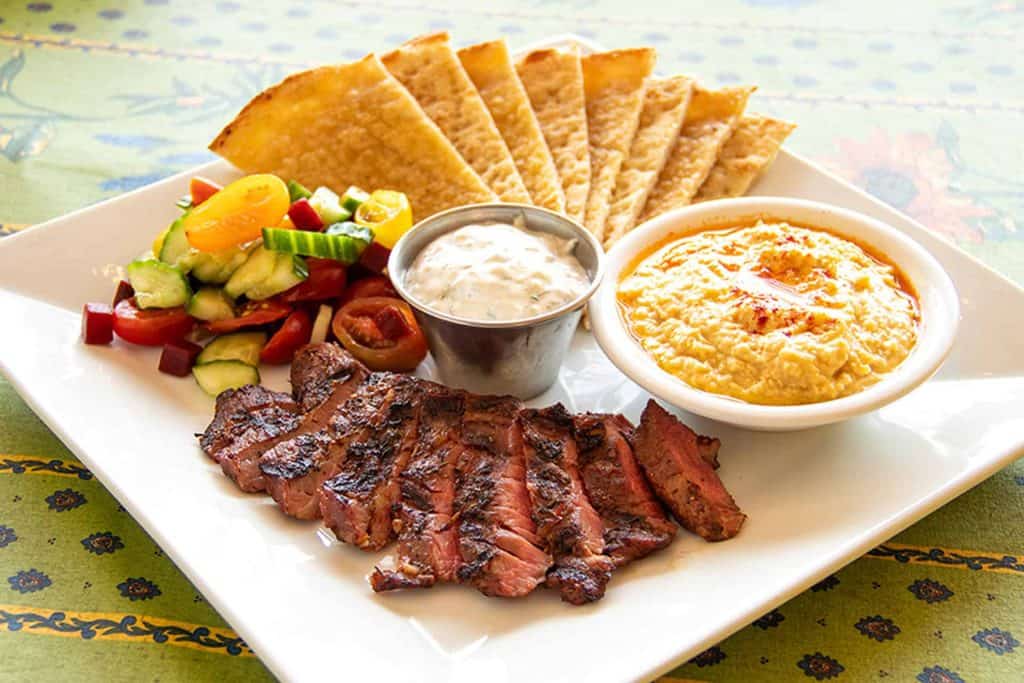 Grilled sirloin steak with hummus, pita chips, and fresh vegetable salad.
