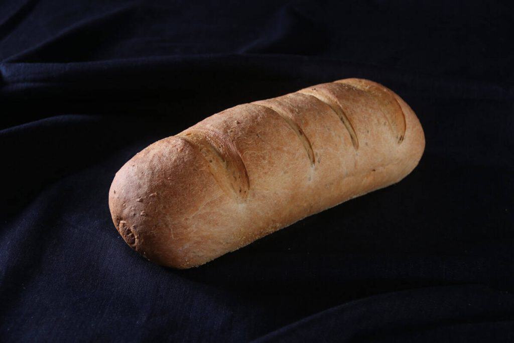 Freshly baked rustic rye bread on black fabric background.