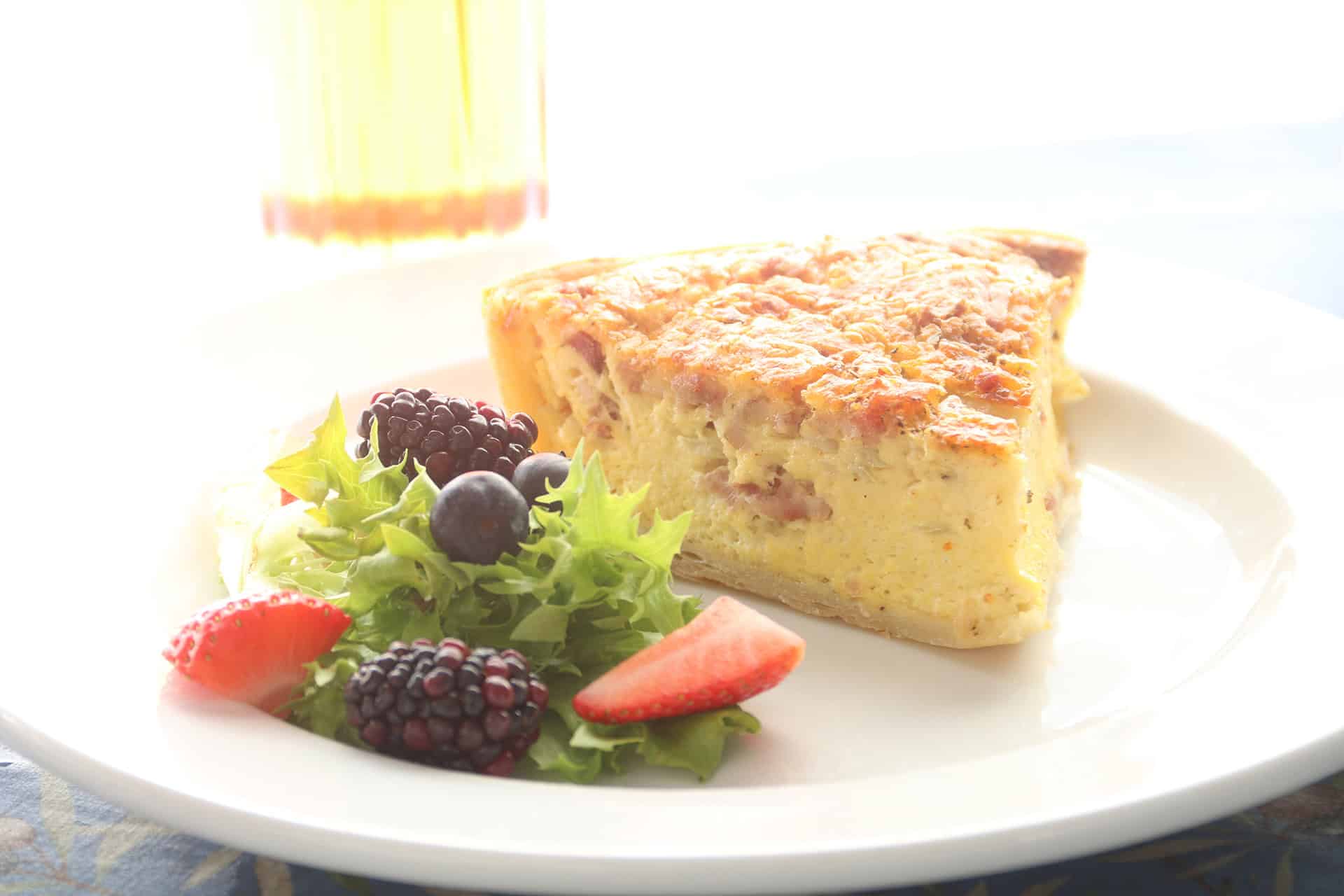 Slice of cheese and berry quiche with fresh greens on white plate.