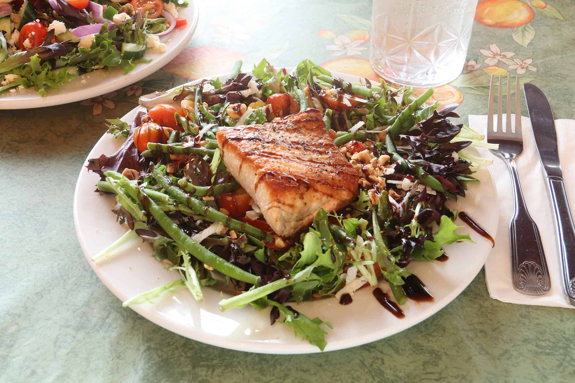 Healthy grilled fish with mixed greens and vegetables on a white plate.