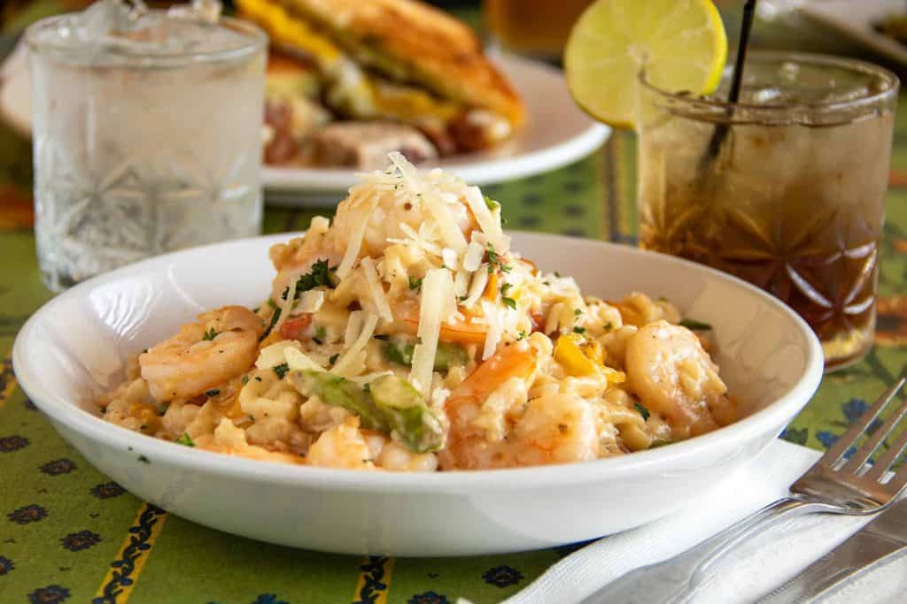 Shrimp spaetzle dish with cheese and herbs, lemon wedge, and drinks on the table.