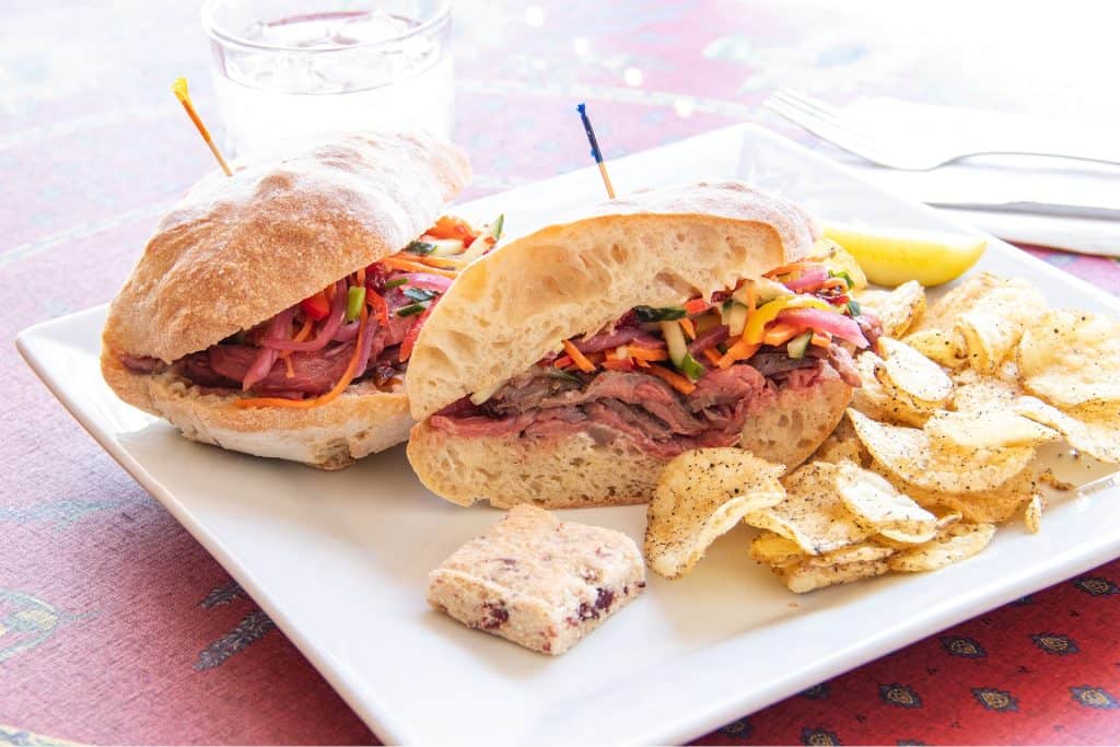 Delicious blackened grouper sandwich with fresh vegetables and crispy chips on a white plate.