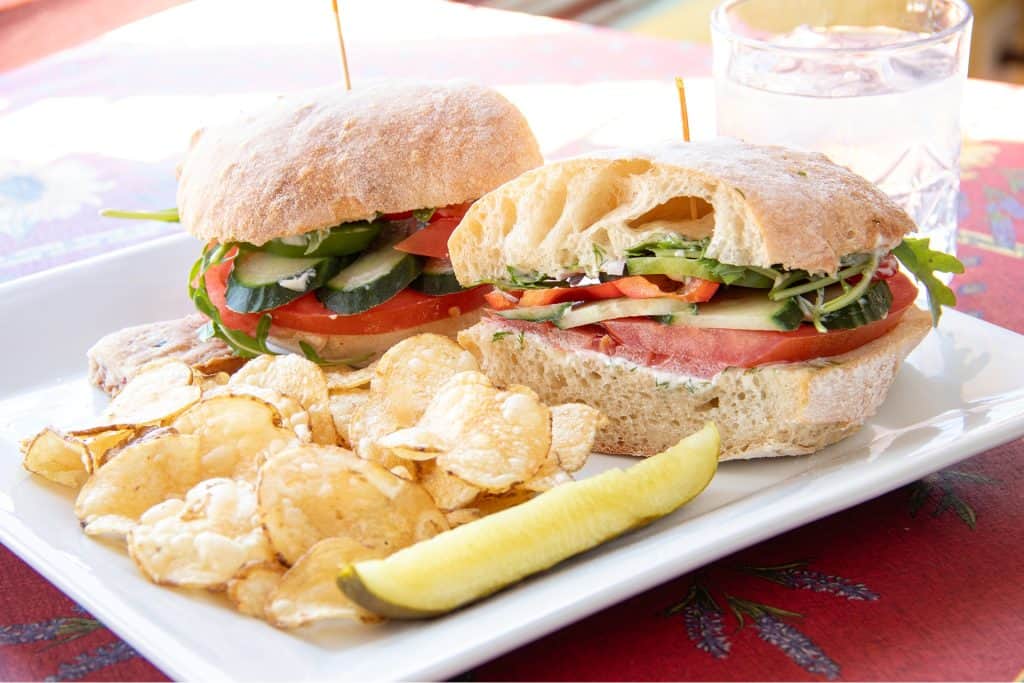 Fresh Village Baker sandwich with vegetables and chips on a white plate.