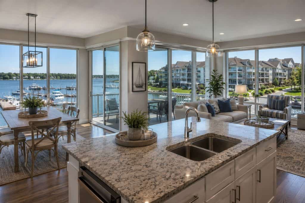 Bright waterfront living room with large windows and modern kitchen.
