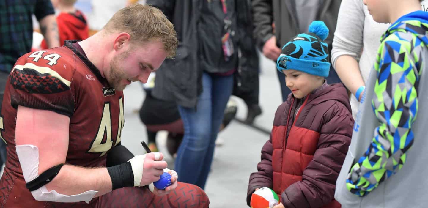 West Michigan Ironmen football player signing autographs for young fans at a community event.