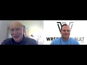 Two men in a video call, one smiling, with Wrestling Vault logo in background.