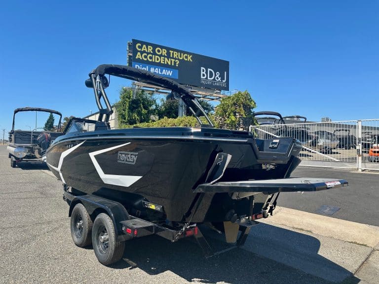 Black boat on trailer at marina with dealership signage in background.