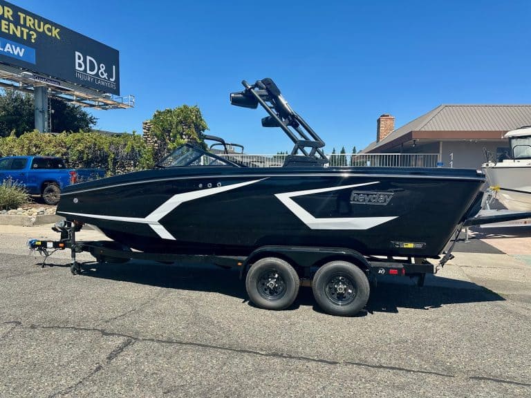 Black and white boat on trailer at dealership lot under blue sky.