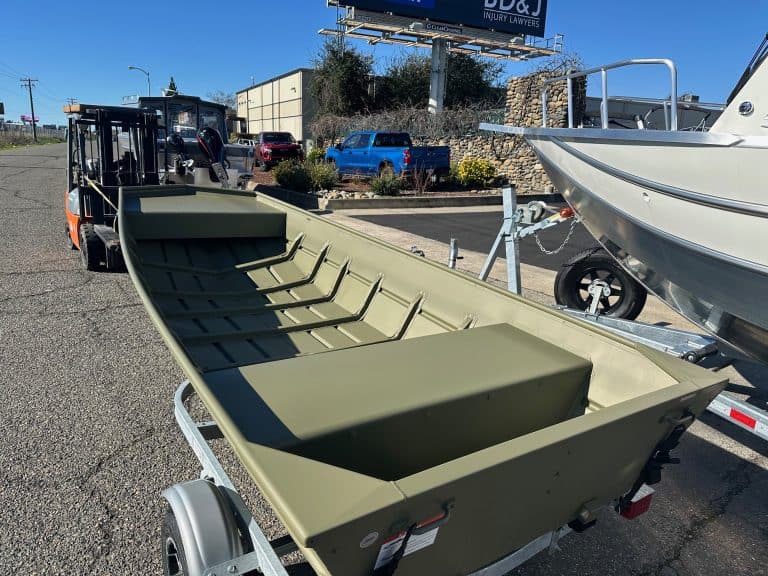Aluminum fishing boat on trailer with open deck and seating.