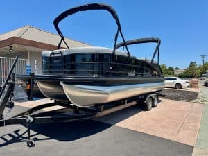 Pontoon boat on trailer ready for water, featuring sleek black and silver design for leisure boating.