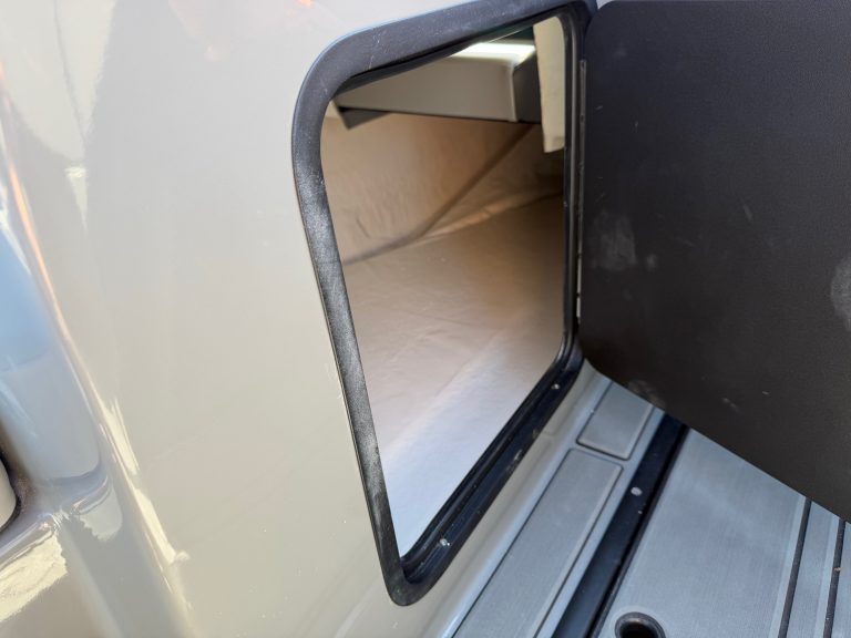 Open storage compartment on a boat with a black lid and beige interior.