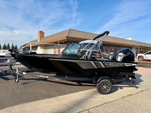 Lowe FM 1775 WT boat with Mercury 115HP engine on trailer, parked outside a dealership under a blue.