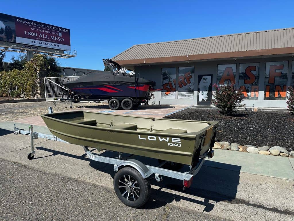 Lowe 1040 fishing boat on trailer outside surf shop with mural background.