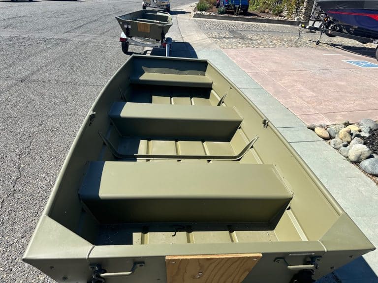 Boat with storage compartments for fishing or recreation, parked near a sidewalk.
