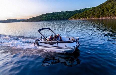 Boat cruising on a lake with lush green hills in the background.