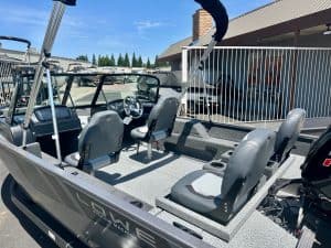 Pontoon boat with seating and steering console at a marina.