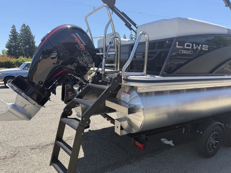 Lowe pontoon boat with outboard motor and boarding ladder on trailer.