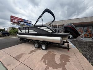 Pontoon boat with outboard engine on trailer, ready for sale or transport.