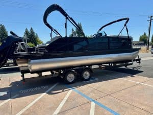 Luxury pontoon boat with black and silver design on trailer in parking lot.