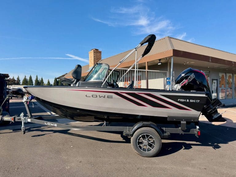 Lowe Fish & Ski boat with outboard motor on trailer at dealership.