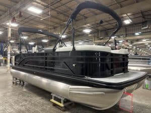 Pontoon boat with black canopy and sleek design in indoor showroom.