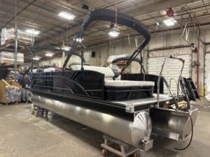 Luxury pontoon boat with black and white design, ready for deployment, in a manufacturing warehouse.