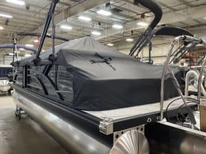 Pontoon boat with protective cover in a manufacturing facility.
